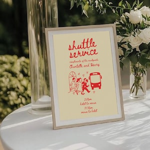 Può includere: Un cartello incorniciato con le parole "shuttle service" in rosso. Il cartello include un'illustrazione rossa di persone e un autobus, con testo che indica l'orario della navetta. Il cartello è su un tavolo bianco.