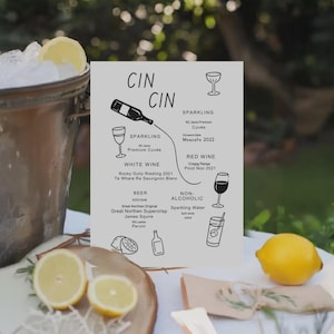May include: A drinks menu with the words "CIN CIN" at the top, listing sparkling, white, and red wines, beer, and non-alcoholic options. The menu is on a white background, with illustrations of glasses and bottles. Sliced lemons and a bucket of ice are in the foreground.