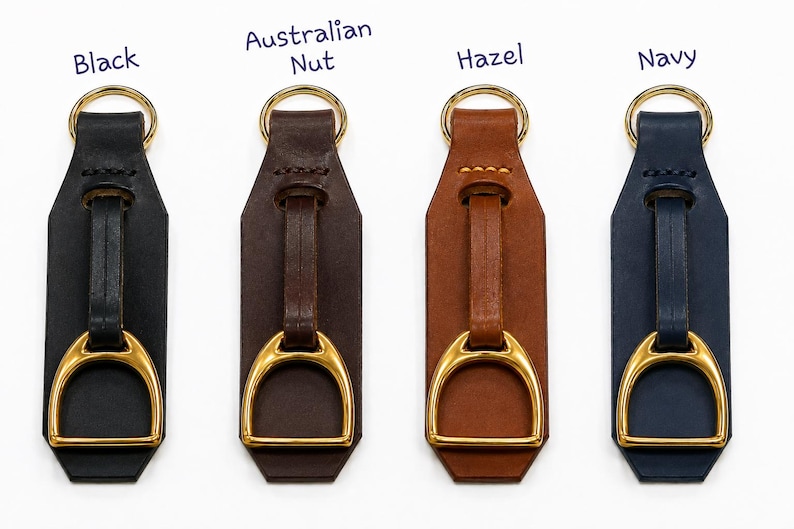 May include: Four leather keychains in black, Australian Nut, hazel, and navy colours. Each keychain features a gold-toned metal stirrup accent attached to a leather strap and a gold-toned circular ring at the top for attachment to keys or bags.