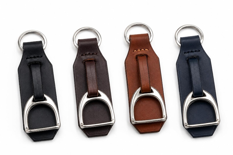 May include: Four leather keyrings in black, dark brown, tan, and navy blue. Each keyring features a silver-toned metal stirrup attached to a leather strap with a matching silver-toned metal split ring at the top for securing keys.
