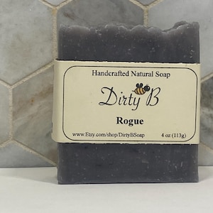 Puede incluir: Una pastilla de jabón gris oscuro con una etiqueta blanca que dice "Jabón natural artesanal Dirty B Rogue 4 oz (113g) www.Etsy.com/shop/DirtyBSoap"