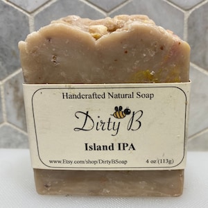 May include: A bar of handcrafted natural soap with a beige colour and a label that reads "Dirty B Island IPA 4 oz (113g) www.Etsy.com/shop/DirtyBSoap".