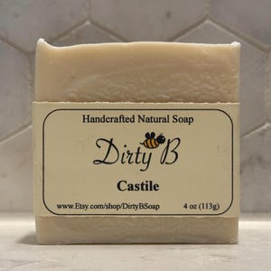 Peut inclure: Une barre de savon naturel artisanal blanc avec une étiquette qui indique "Dirty B Castile" et "4 oz (113g)". L'étiquette comprend également une abeille de dessin animé et l'adresse du site Web "www.Etsy.com/shop/DirtyBSoap".