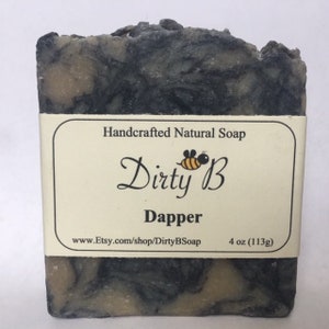 May include: A bar of handcrafted natural soap with a black and white marbled design. The soap is labeled "Dirty B Dapper" and has a bee logo. The soap weighs 4 oz (113g).