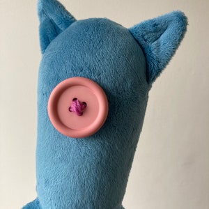May include: A blue plush toy with a pink button for an eye and two floppy ears. The toy has a long body and multiple tentacles.