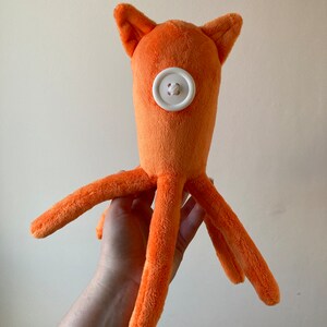 May include: Orange plush octopus toy with a white button for an eye.