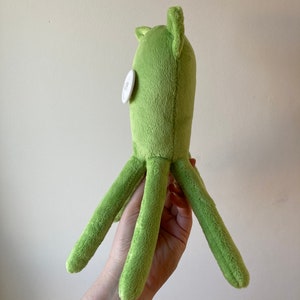 May include: A green plush octopus with a white button eye. The octopus has six tentacles.