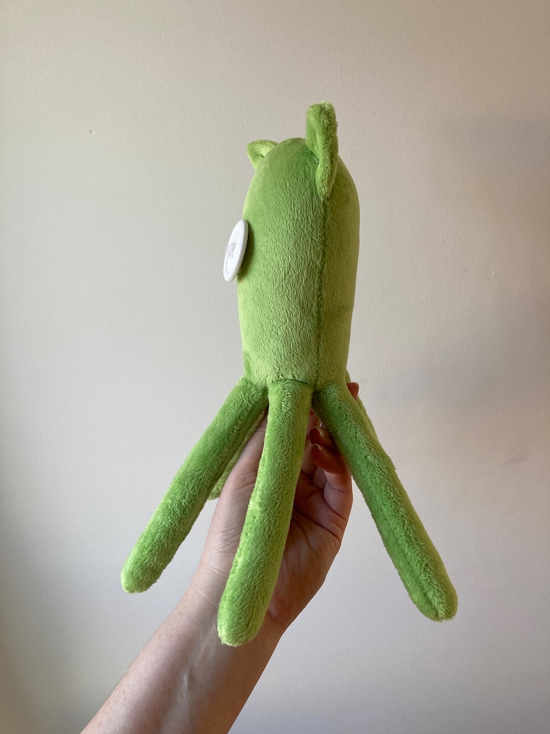 May include: A green plush octopus with a white button eye. The octopus has six tentacles.