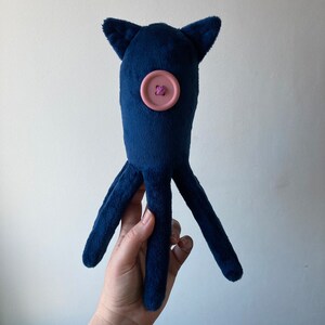 May include: A plush blue octopus toy with a pink button for an eye. The octopus has four tentacles.