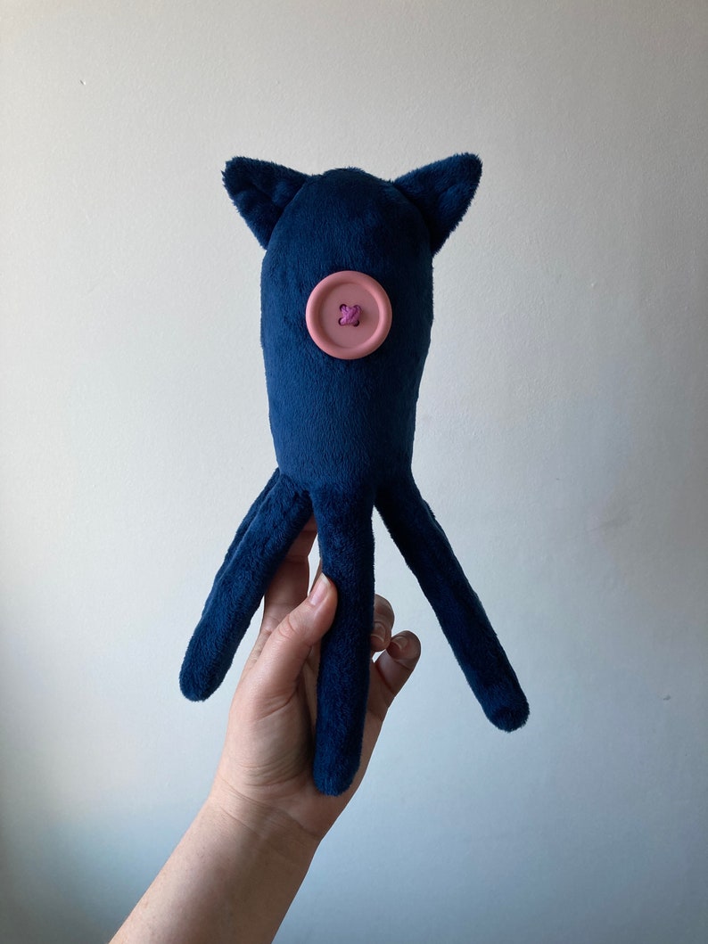 May include: A plush blue octopus toy with a pink button for an eye. The octopus has four tentacles.