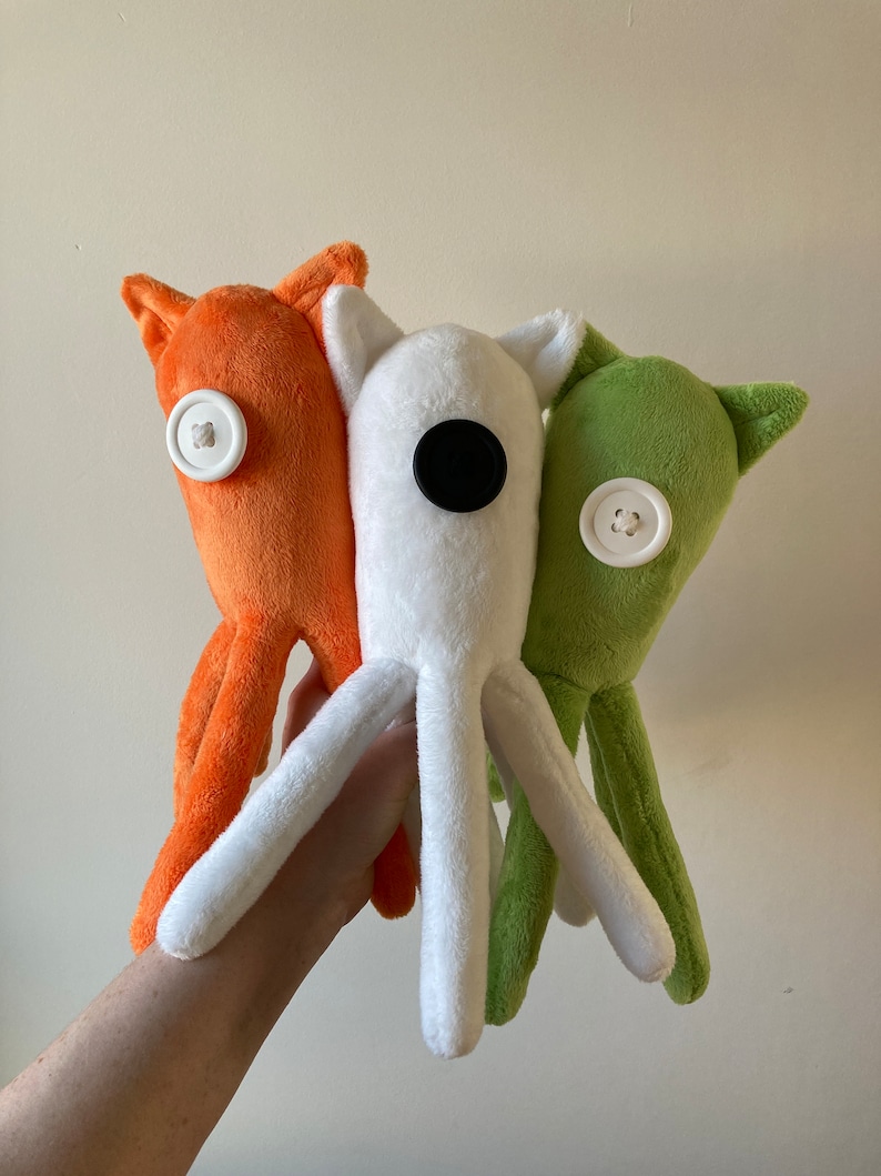 May include: Three plush toys shaped like octopus with different colored bodies. The octopus on the left is orange, the middle octopus is white, and the octopus on the right is green. Each octopus has a button for an eye.