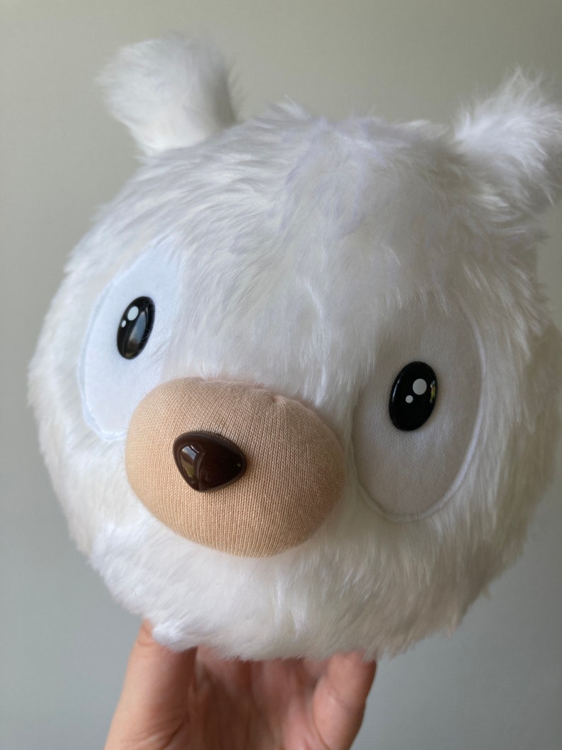 Puede incluir: Juguete de peluche blanco con cabeza redonda, ojos negros y nariz marr&oacute;n. El juguete est&aacute; hecho de un material suave y esponjoso.