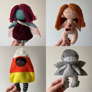 May include: Four handmade felt dolls. A red-haired doll with a white dress and a red heart on her chest. A blue-haired doll with a red dress and a white cape. A candy corn doll with a yellow, orange, and white costume. A gray monster doll with a white mouth and wings.