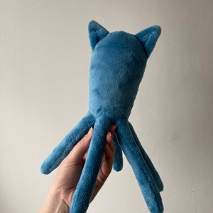May include: A blue plush octopus with long, thin tentacles and two small ears on top of its head.