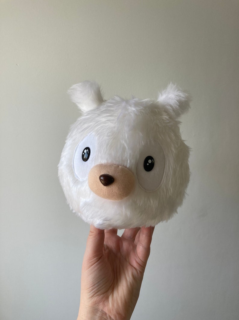 Puede incluir: Juguete de peluche blanco con forma de cabeza de oso con ojos negros, nariz marr&oacute;n y cuerpo blanco y esponjoso.