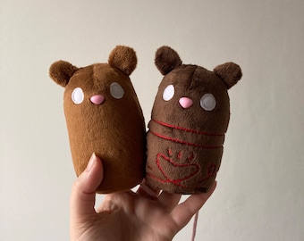 Könnte beinhalten: Zwei braune Plüschmausspielzeuge. Eine Maus hat ein schlichtes Design, die andere rote Nähte und ein Herzdesign.