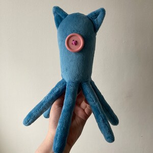May include: A blue plush octopus toy with a pink button for a nose. The octopus has six tentacles.