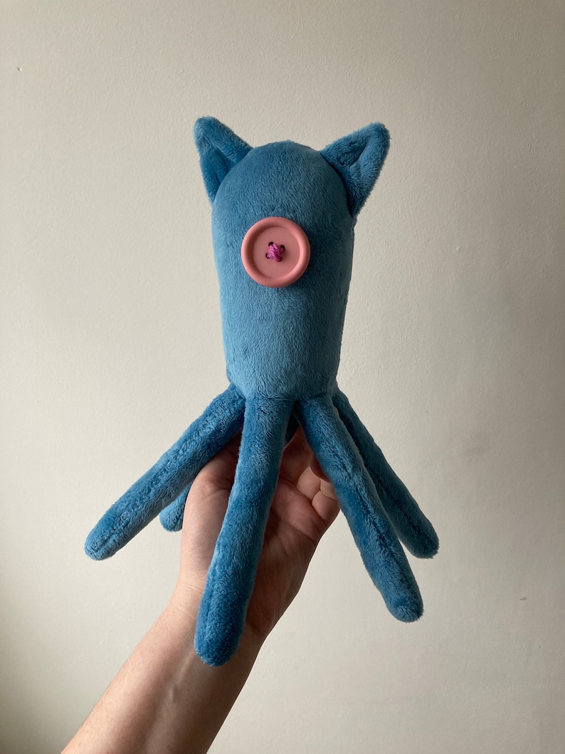 May include: A blue plush octopus toy with a pink button for a nose. The octopus has six tentacles.