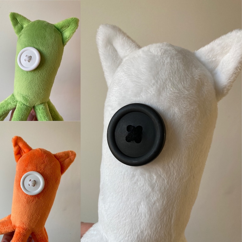 May include: Three plush toys with button eyes. The first is green with a white button, the second is white with a black button, and the third is orange with a white button.