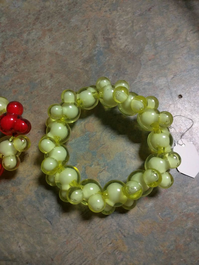 May include: A yellow beaded bracelet with a white tag attached. The beads are round and have a translucent appearance.