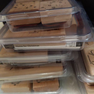 May include: A set of three clear plastic containers with wooden stamps inside. The stamps are labeled "Home for Christmas". The containers are stacked on top of each other. The top container has a label that says "Set of/Ensemble de/Juego de/Satz von 3"