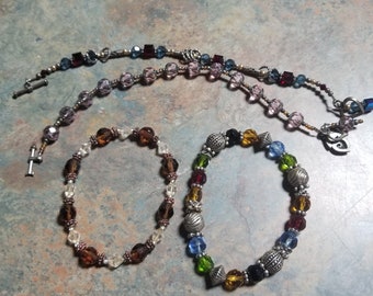 May include: Three beaded bracelets with silver accents. The top bracelet has pink, blue and red beads. The middle bracelet has brown and clear beads. The bottom bracelet has green, blue and gold beads.