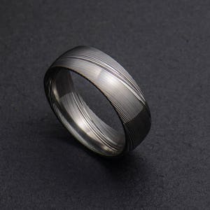 May include: A silver ring with a unique, patterned design. The ring is made of metal and has a smooth, polished finish.
