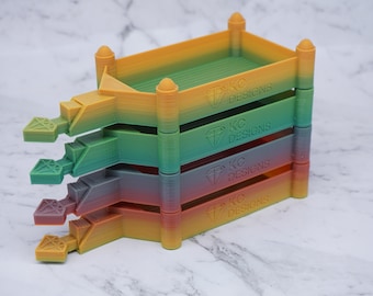 May include: Four stacked rainbow-colored plastic trays with a diamond logo and the text "KC Designs" on each. The trays are designed for organizing small items.