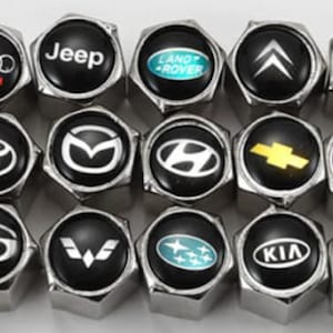 May include: A selection of black and silver car tyre valve stem caps, each displaying a different car brand logo in white or colour. Brands include VW, Audi, Jeep, Land Rover, and others.