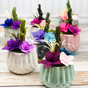 May include: A collection of five small potted plants with colorful paper flowers. The pots are decorated with geometric patterns and the flowers are in shades of pink, purple, blue, and green.