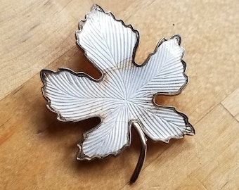 May include: A silver-toned leaf-shaped brooch with a textured surface. The leaf has a pointed tip and a stem.