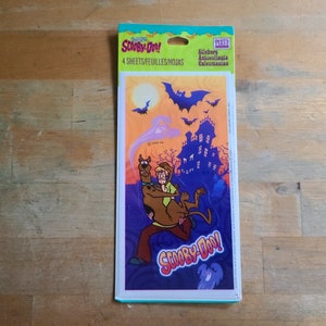 May include: A package of Scooby-Doo! stickers featuring Scooby and Shaggy running from a haunted house with bats flying overhead. The package says "Scooby-Doo!" and "4 sheets/feuilles/hojas".