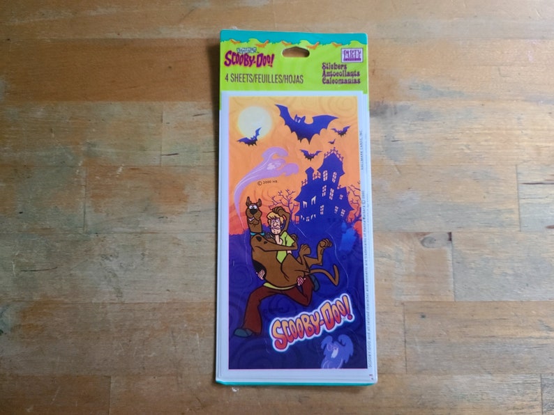 May include: A package of Scooby-Doo! stickers featuring Scooby and Shaggy running from a haunted house with bats flying overhead. The package says "Scooby-Doo!" and "4 sheets/feuilles/hojas".