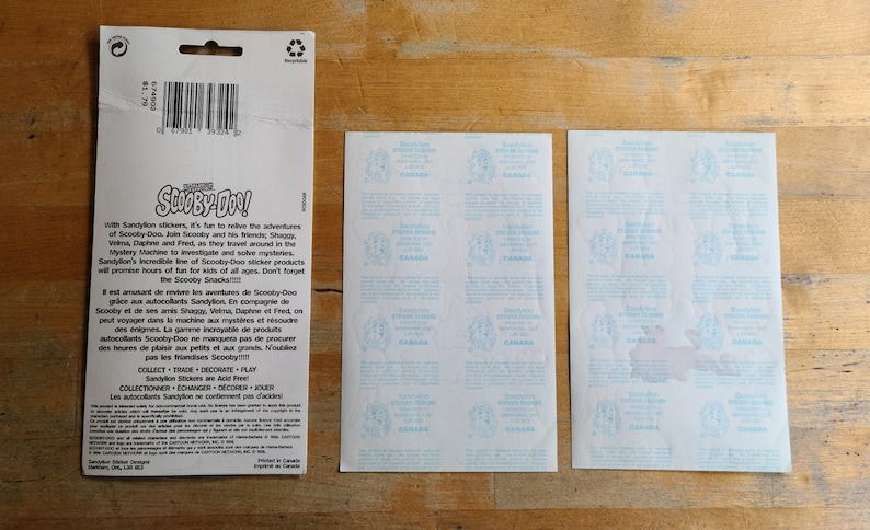 May include: A sheet of Scooby-Doo stickers featuring the Mystery Machine and the Scooby-Doo gang. The stickers are on a white background with blue text. The back of the sheet has instructions for using the stickers in English and French.