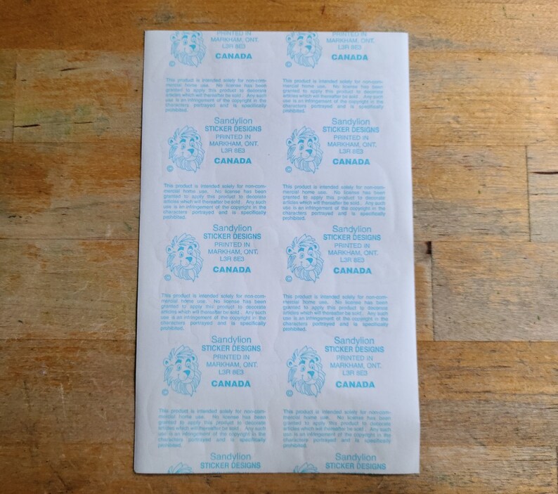 May include: A sheet of stickers with a lion logo and the text "Sandylion Sticker Designs Printed in Markham, ONT L3R 8E3 Canada".