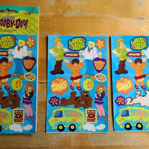 May include: Three sheets of Scooby-Doo stickers featuring the characters from the show. The stickers are on a blue background with the text "Like Wow!" and "Coinks".