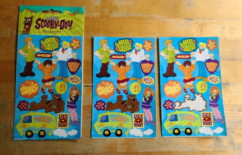 May include: Three sheets of Scooby-Doo stickers featuring the characters from the show. The stickers are on a blue background with the text "Like Wow!" and "Coinks".