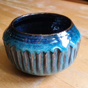 May include: A handmade ceramic bowl with a textured, ridged exterior. The bowl features a gradient of blue and turquoise glazes, with a dark blue interior. The bowl is approximately 4 inches in diameter and 3 inches tall.