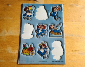 May include: A sheet of vintage stickers featuring a cartoon girl with red hair in various poses. The stickers are on a light blue background with white cut-out shapes. The stickers include the text "© 1981 BERRIE & CO. INC."