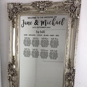 Peut inclure: Un miroir encadré argent avec un plan de table de mariage. Le plan liste les noms des invités assignés à chaque table. Le haut du plan indique "Bienvenue au mariage de Jane & Michael 25 septembre 2002".