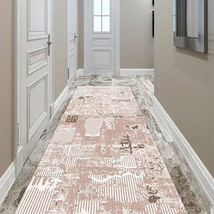 Puede incluir: Una alfombra de pasillo rectangular con un diseño abstracto desgastado en tonos rosa y blanco. La alfombra presenta un patrón de rayas verticales y elementos texturizados. La alfombra está hecha de un material suave y añade interés visual al pasillo. Mide unos 200 cm de largo.