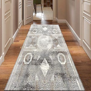 Puede incluir: Una alfombra rectangular para pasillo con un patrón geométrico en tonos grises y blancos. La alfombra presenta formas de diamantes y circulares, creando un diseño simétrico. La alfombra está colocada sobre un suelo de madera.