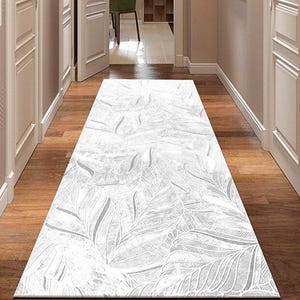 Puede incluir: Una alfombra de pasillo con estampado blanco y gris con diseño de hojas sobre un suelo de madera. El diseño de la alfombra presenta un patrón repetido de hojas estilizadas.