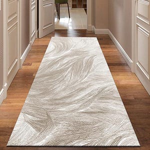 Puede incluir: Una alfombra larga y rectangular con un patrón fluido y texturizado en tonos beige y blanco roto. La alfombra está colocada en un pasillo con suelo de madera y puertas blancas, creando una estética neutra y acogedora.