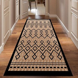 May include: A rectangular hallway rug with a geometric pattern. The rug features a tan background with black diamond and zigzag designs. The border is black, and the rug is placed on a wooden floor.