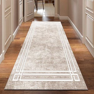 May include: A rectangular, light beige hallway rug with a geometric border design. The rug is placed on a dark wood floor, and the hallway is flanked by white doors and walls. The rug measures approximately 244 cm long.