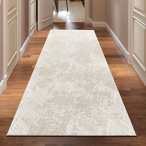 Puede incluir: Un pasillo con una alfombra beige claro texturizada. La alfombra tiene un patrón sutil y está sobre un suelo de madera. Puertas y molduras blancas bordean las paredes, y una puerta conduce a una habitación con una silla verde.