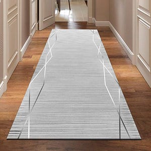 May include: A rectangular gray and white patterned rug with geometric silver lines, placed on a wooden floor in a hallway. The rug's design features horizontal stripes and a modern aesthetic, enhancing the space.