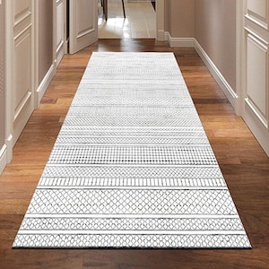 Puede incluir: Una alfombra de pasillo con estampado blanco y gris en un pasillo con suelo de madera. La alfombra presenta varios diseños geométricos y rayas. El pasillo tiene puertas y paredes blancas, con una vista de una silla verde y una ventana al final.