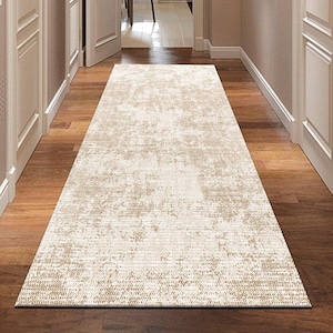 May include: A beige and tan patterned runner rug in a hallway with hardwood floors. The rug has a distressed, abstract design and is centered in the hallway. White doors and trim are visible on either side.
